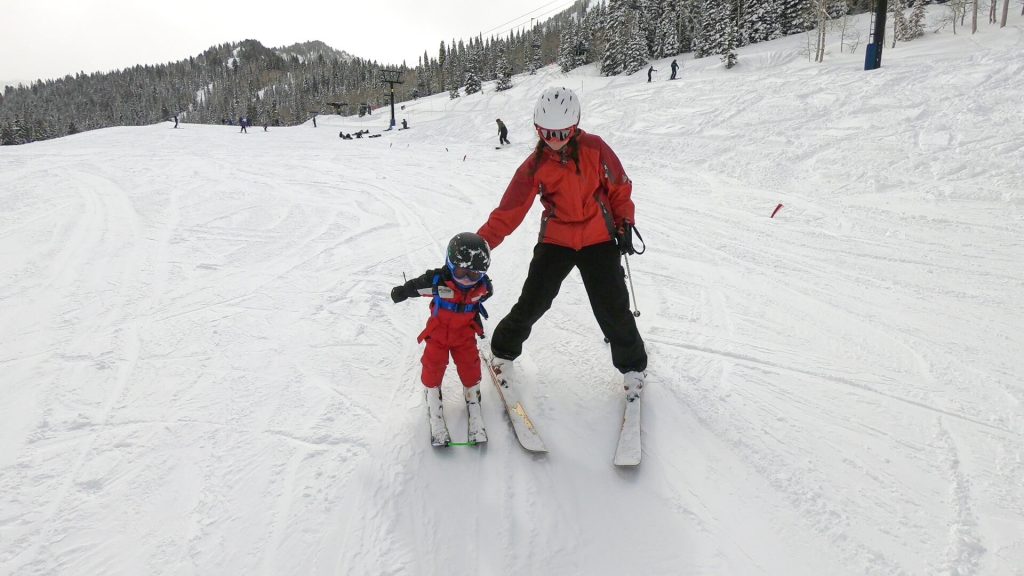 Skiing Kids mom pushing toddler on skis with edgie wedgie