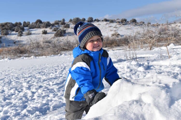 litle boy playing in the snow wearing a winter hat